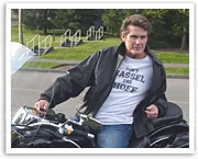 Man in a leather jacket sitting on a motorcycle, wearing a "Don't Hassel the Hoff" T-shirt.