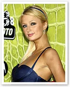 Blonde woman in a blue dress against a green patterned background, posing with a slight smile.