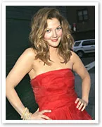 Woman in a strapless red dress poses with hands on hips, smiling, against an outdoor backdrop.