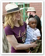 Madonna holding a young child in her arms, wearing a purple shirt and straw hat, with others in the background.