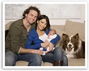 Family sitting on a couch with a baby and a dog, smiling and posing for the camera.