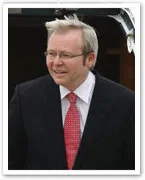 A man in a suit and red tie, with glasses and light hair, standing outdoors and smiling.