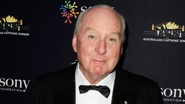 A person in a tuxedo at the Australian Captains' Dinner event, standing against a backdrop with logos.