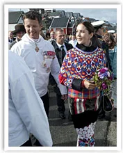 A woman wearing a colorful traditional Inuit outfit holds flowers in a crowd, with others dressed in formal attire nearby.