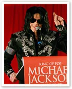 Michael Jackson at a press conference wearing a black embellished jacket and sunglasses, speaking at a podium.