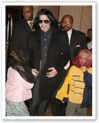 Michael Jackson in a black coat and sunglasses, surrounded by security, with two children wearing veils over their faces.
