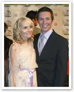 Two people smiling at a formal event; the woman is in a light dress, and the man is in a suit.