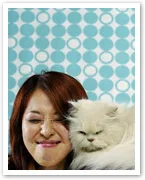 Young woman smiling with eyes closed, leaning against a fluffy white cat, with a blue circular pattern background.