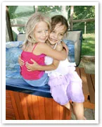 Two young girls hugging each other while sitting on the edge of a hot tub in an outdoor setting.