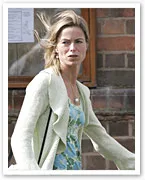 Woman in light cardigan and floral dress walking outdoors with a serious expression.