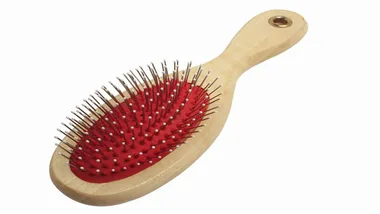 Wooden hairbrush with red cushion and metal bristles, angled view on a white background.