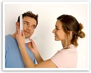 A woman playfully measures a man's face with a tape measure, both smiling.
