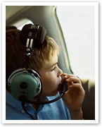 Child looking out airplane window, wearing aviation headset, thoughtful expression.