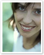 Smiling woman with brown hair and green eyes, wearing a white shirt, set against a blurred green background.