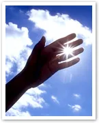 A hand reaching towards the sky, with sunlight shining through the fingers against a backdrop of blue sky and clouds.