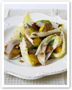 Endive salad with turkey, pecans, and oranges on a white plate.
