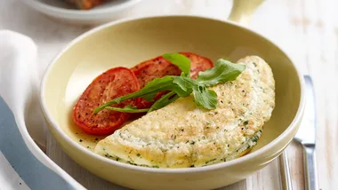 Omelette with herbs topped with arugula, served alongside roasted tomatoes on a beige plate.
