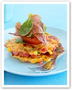 Vegetable fritters topped with spinach, tomato, and crispy garnish on a blue plate with a fork.