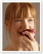 A woman with blonde hair biting into a red apple, smiling.