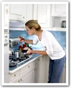 A woman cooking in a modern kitchen, stirring a pot on the stove while focused on her task.