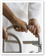 Person using a walker, wearing a white long-sleeve shirt, hands gripping the handles.