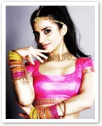 Young woman in traditional Bollywood dance attire with colorful bangles, jewelry, and a pink blouse, posing confidently.