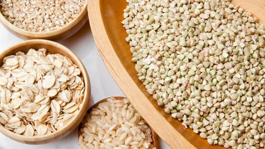 Assorted gluten-free grains in bowls: oats, buckwheat, and brown rice.