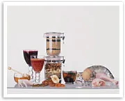 Various foods and drinks, including wine, grains, nuts, chicken, and sauces, are neatly arranged on a white surface.