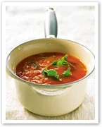 A saucepan filled with tomato soup garnished with fresh coriander on top.