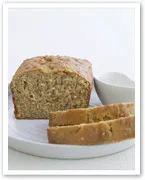 Loaf of whole grain bread with two slices cut, on a white plate with a small white dish.