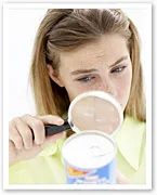 A woman examines a can's label with a magnifying glass, focusing on identifying food additives.