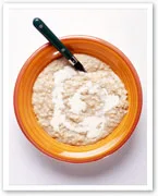 Bowl of oatmeal with milk in an orange bowl, accompanied by a teaspoon.