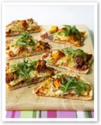 Slices of veggie pizza topped with arugula on a wooden board.