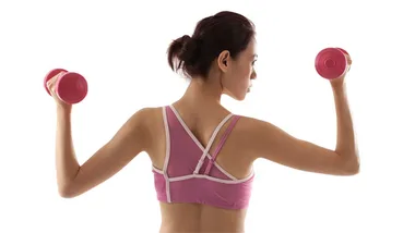 Rear view of a woman in a pink sports bra lifting pink dumbbells, showcasing athletic strength and posture.