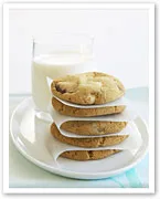 Stack of cookies with parchment sheets on a plate beside a glass of milk.