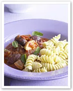 A plate of fusilli pasta with a rich tomato sauce, beef, eggplant, and fresh basil garnishing.