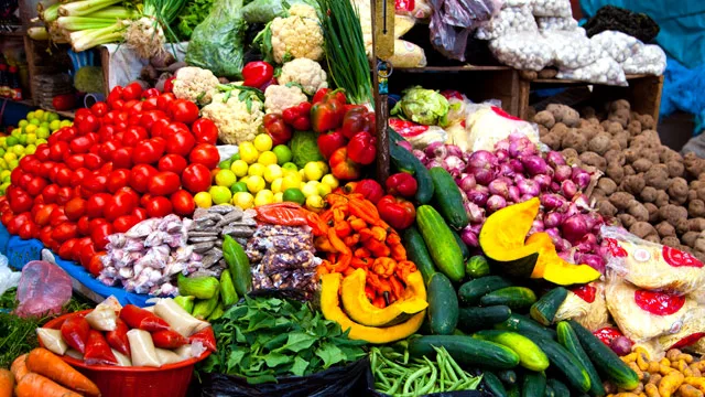 Fresh vegetables and fruits displayed at a market, featuring tomatoes, cucumbers, onions, and cauliflower.