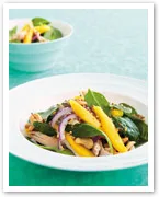 Spinach salad with mango slices, red onion, and almond slivers in a white bowl on a light blue surface.