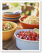 Bowls of colorful salads on an outdoor table, including tomato salsa and a noodle dish.