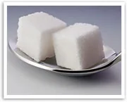 Two sugar cubes on a silver spoon against a neutral background.