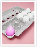 Egg carton with one pink egg among white eggs on a pink background.