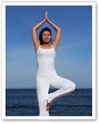 A person in white performs a yoga tree pose on Bondi Beach with a clear blue sky in the background.