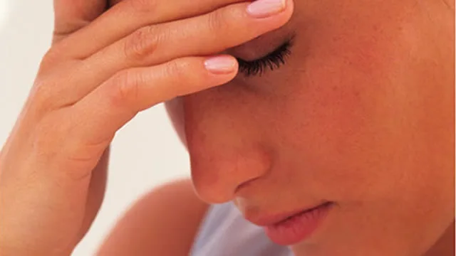 A woman with eyes closed holding her forehead, appearing stressed or anxious.