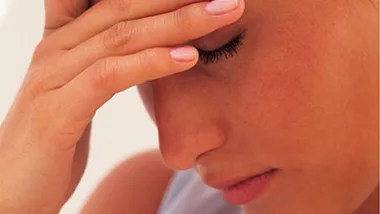 A woman with eyes closed holding her forehead, appearing stressed or anxious.