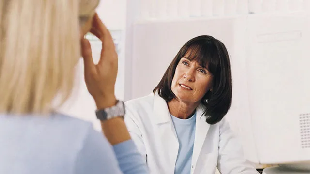 A female doctor attentively listens to a patient in a medical office setting.