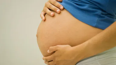 Pregnant woman gently holding her baby bump, wearing a blue top.