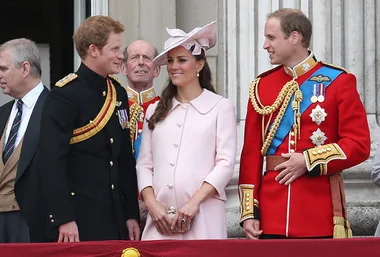 Royal family members in formal attire on a balcony during a ceremonial event, smiling and conversing with each other.