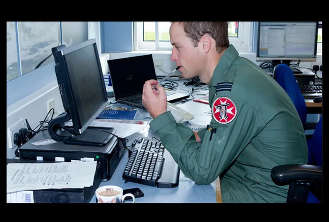 Military personnel in uniform working at a desk with computers and documents; thoughtful expression.