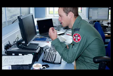 Military personnel in uniform working at a desk with computers and documents; thoughtful expression.