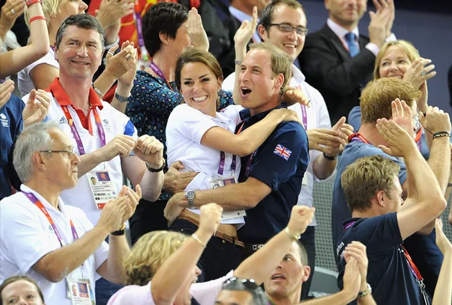 Spectators cheer and embrace at the Olympics, wearing team attire and lanyards, showing excitement and support.